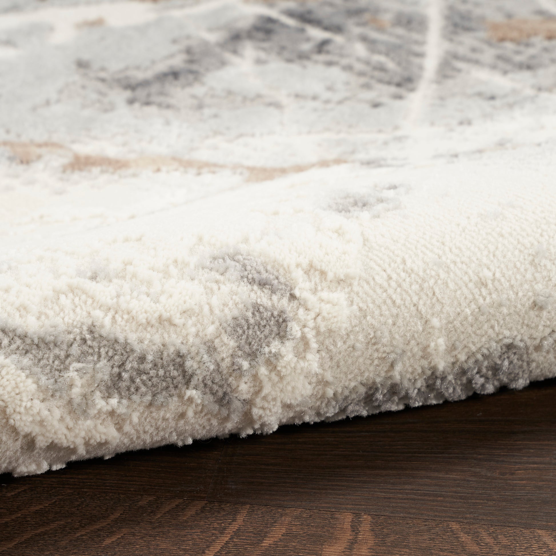 Close-up of a plush cream-gray rug edge with subtle pattern on dark wood floor.