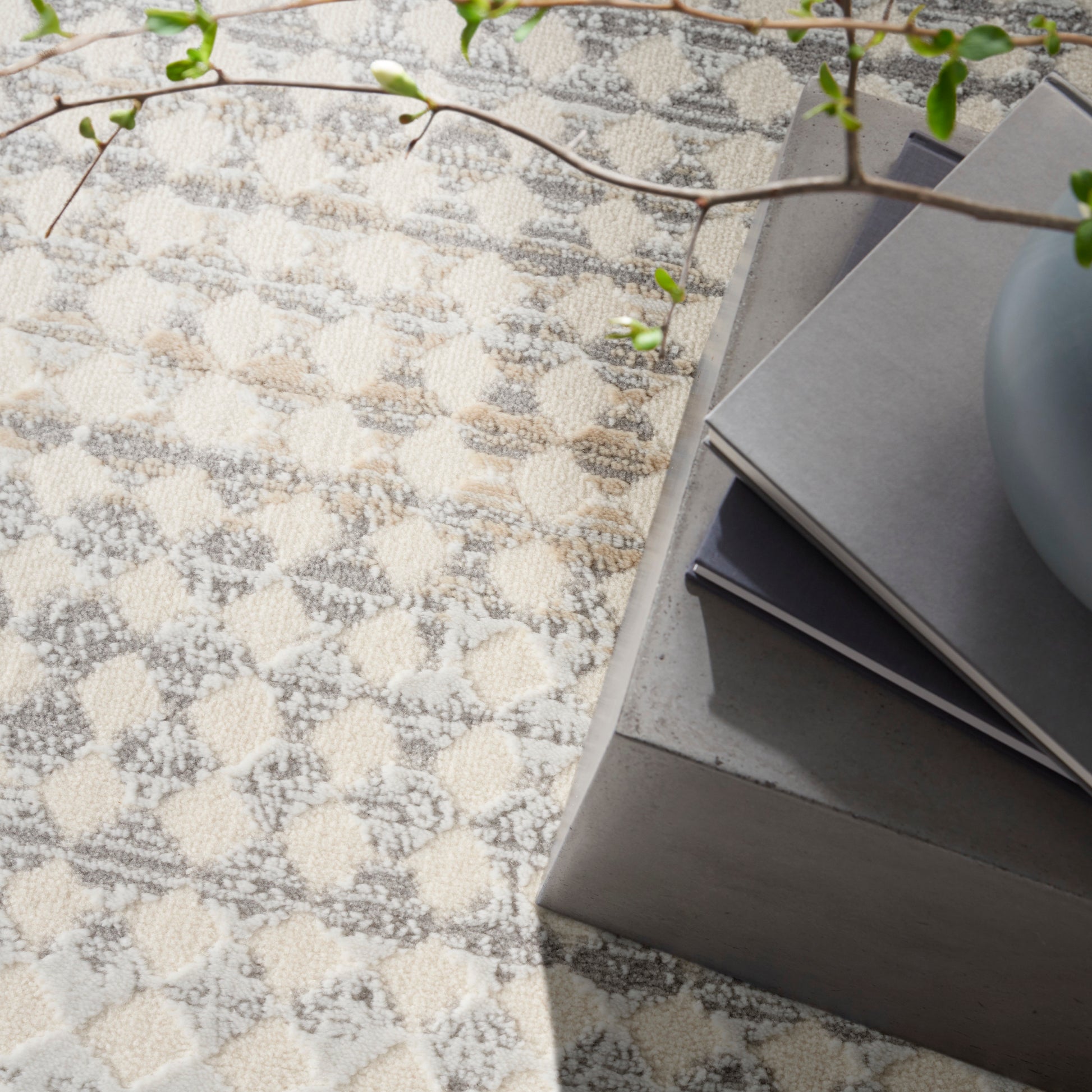 Beige and gray geometric tufted area rug with square motifs beside a concrete coffee table and stacked books.