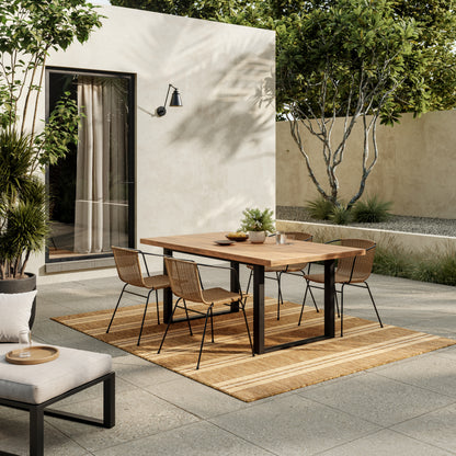 Outdoor dining set with a rectangular wood table and black metal legs, six tan woven chairs on a striped beige rug.