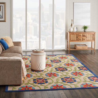 Colorful floral area rug with blue border on dark wood floor; beige sofa, round pouf, and wooden console.