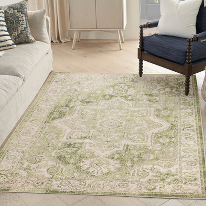 Distressed sage green and ivory oriental-style area rug on a light wood floor, with beige sofa and navy armchair.
