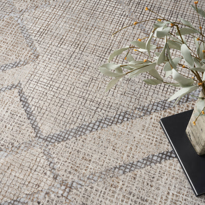 Beige textured rug with gray diamond lattice, eucalyptus stems in a pale vase atop a dark book.