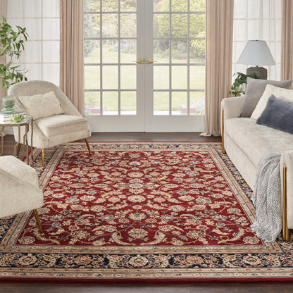 Red Persian-style area rug with ivory border and floral motifs in a beige living room with sofas and French doors.