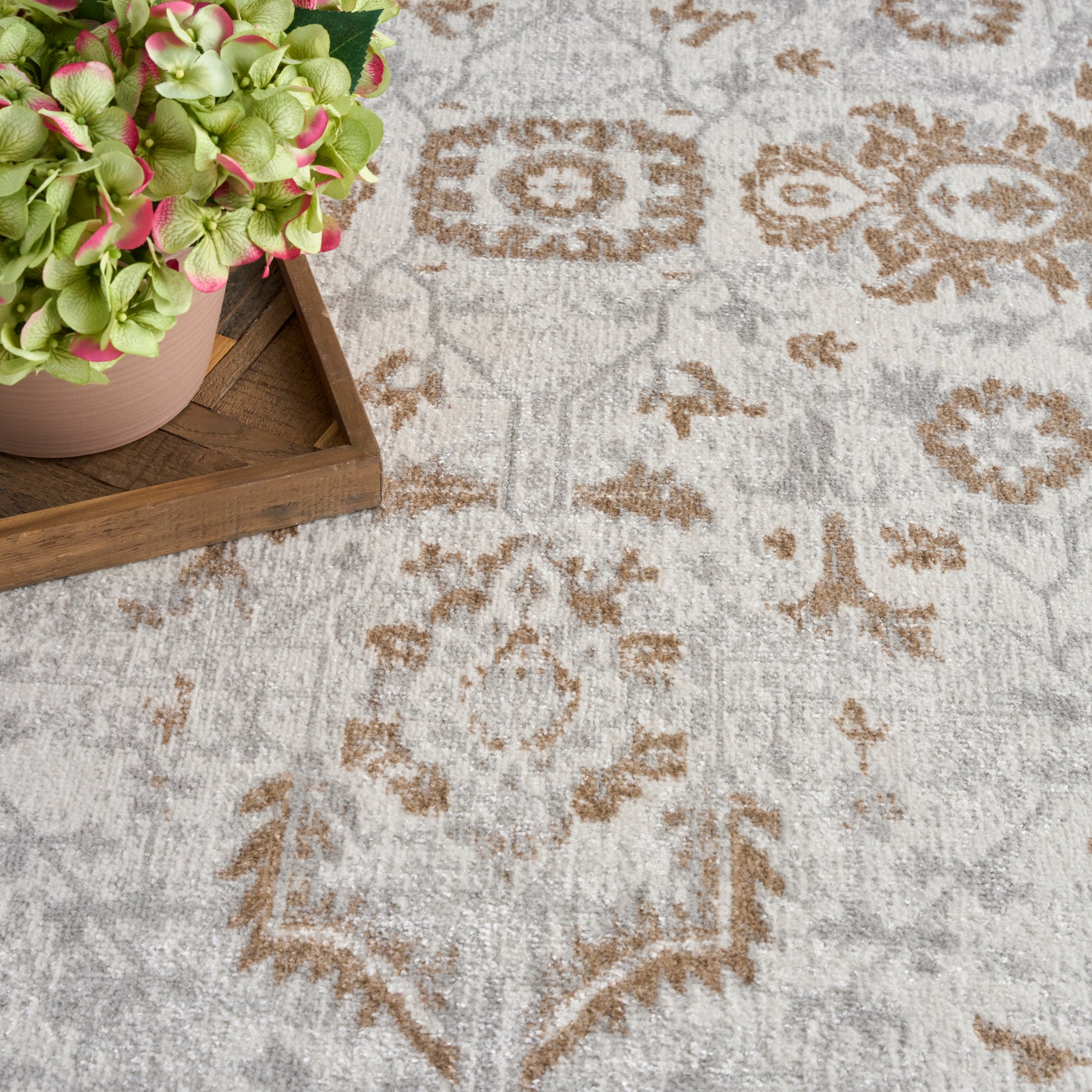 Neutral patterned rug with beige-gray tones and brown ornate motifs; pink-green hydrangea on a wooden tray.