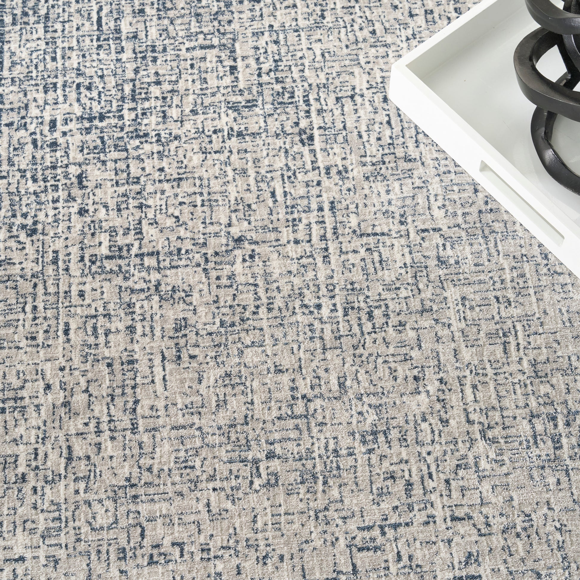Blue and beige abstract patterned area rug with a white tray and a black curved sculpture in the corner.
