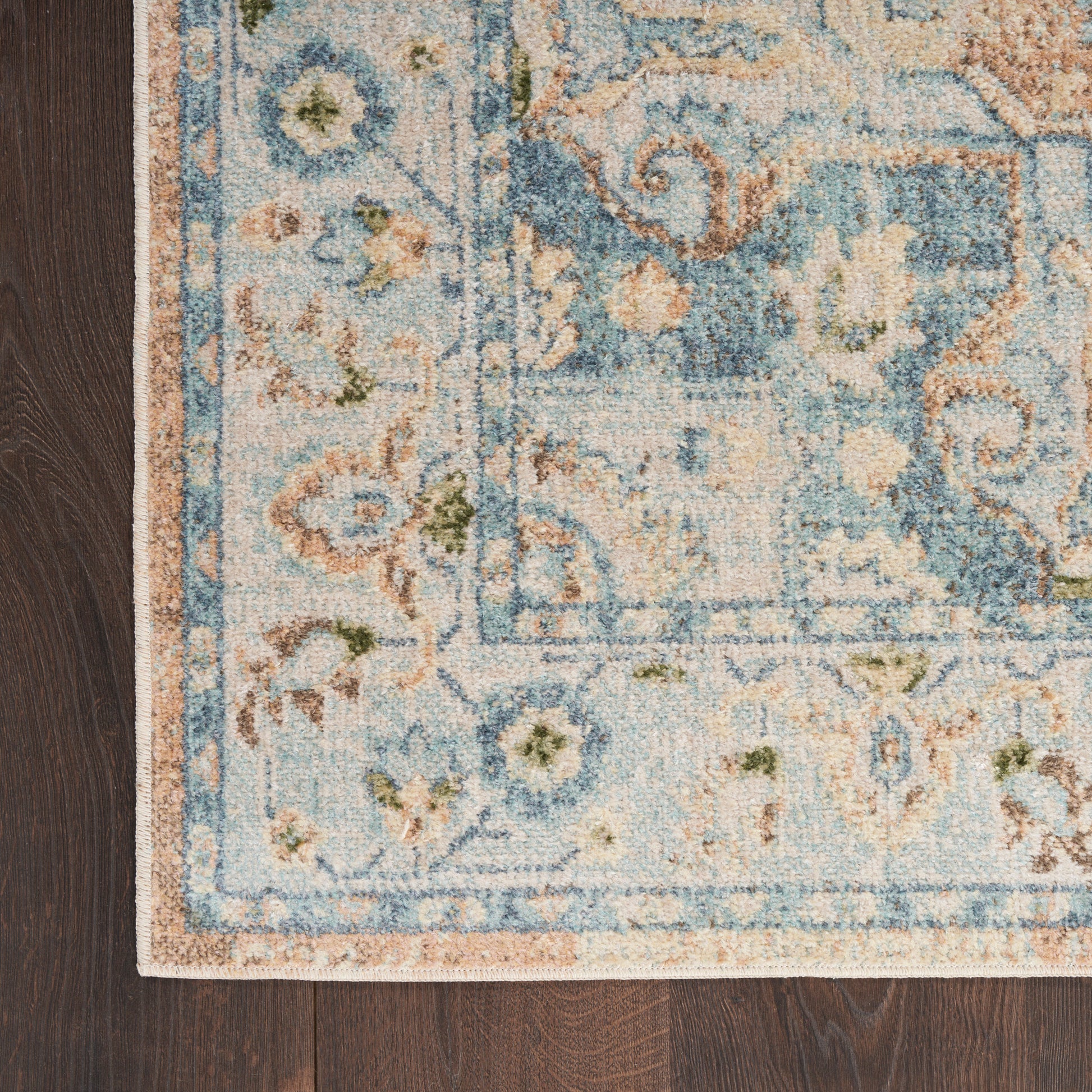 Blue and ivory distressed traditional area rug with floral border on dark wood floor.
