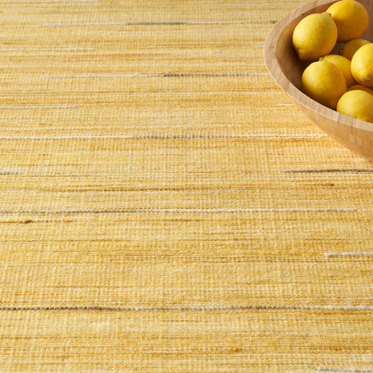 Round wooden bowl of lemons sits on a golden-yellow woven placemat atop a wooden table.