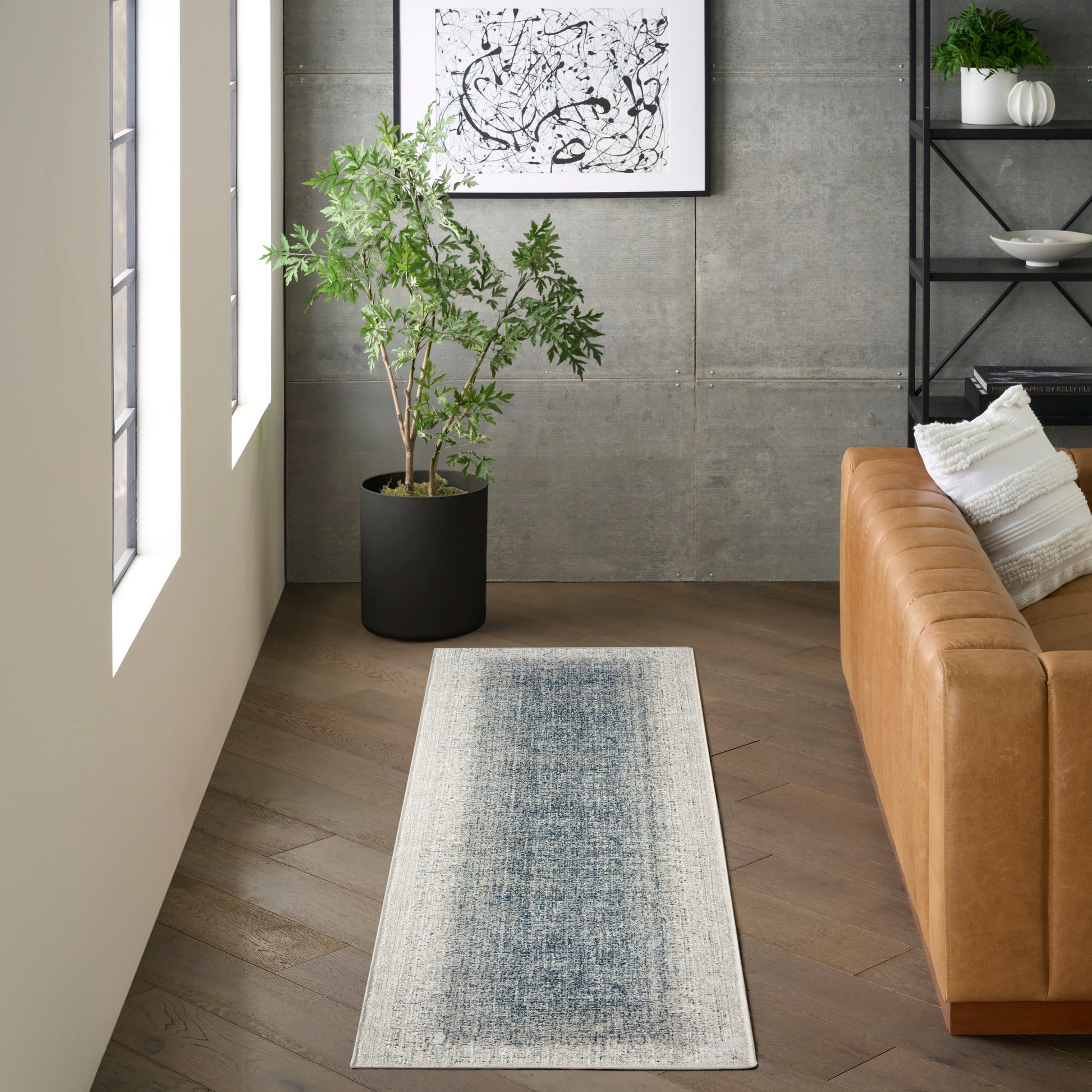 Long blue-gray gradient runner rug with beige border in a modern living room beside a tan leather sofa.