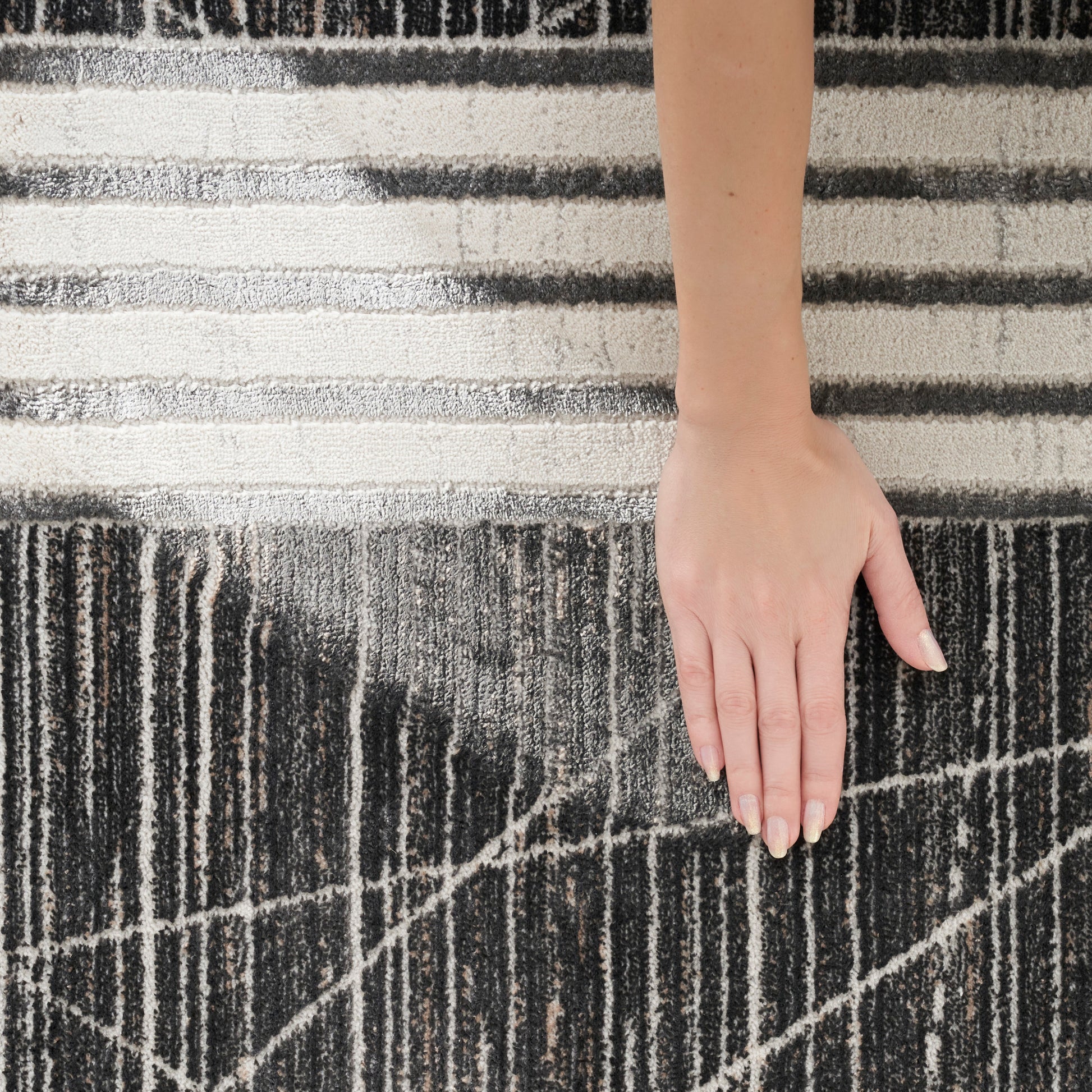Light-skinned hand on a black-and-white striped shag rug with a textured geometric pattern.