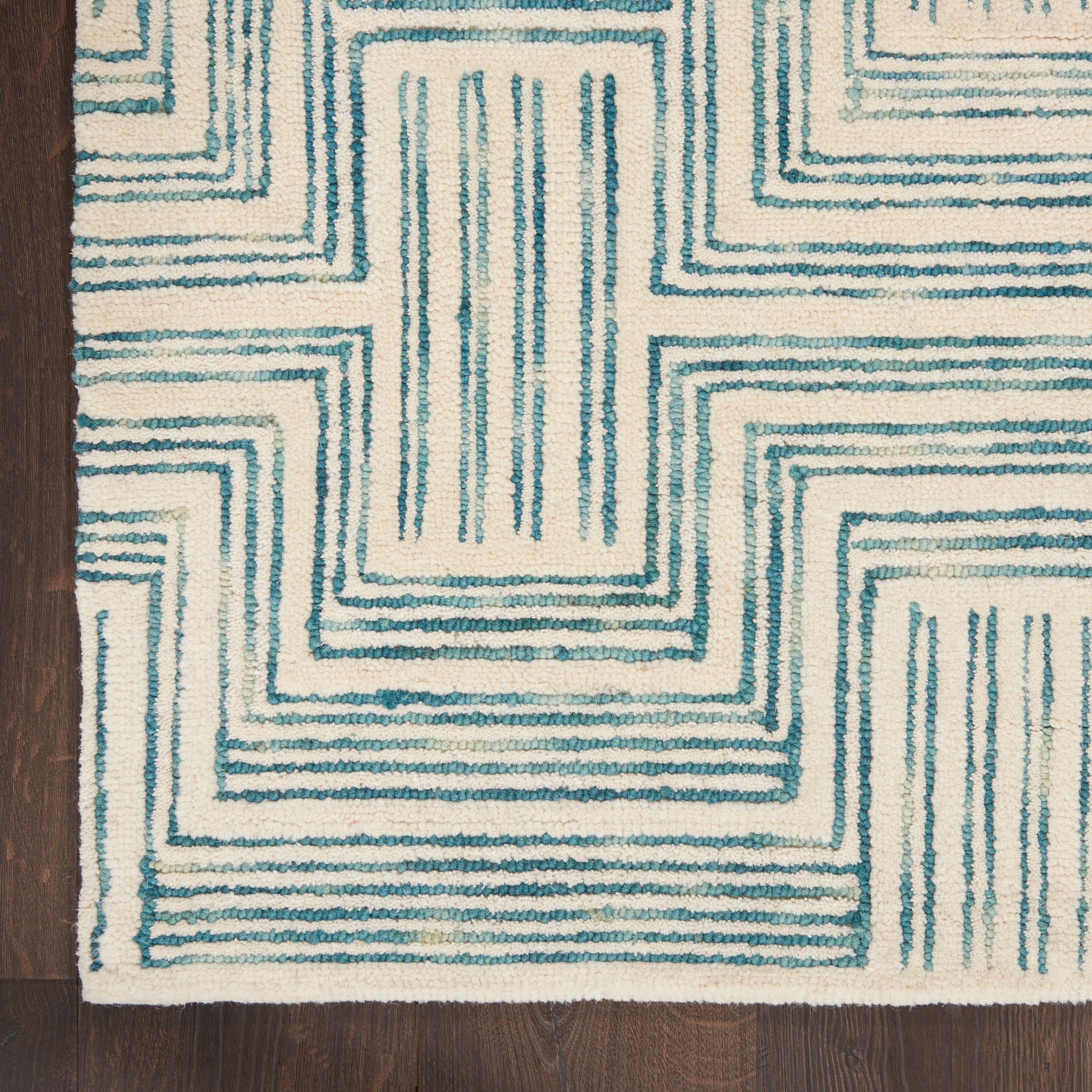 Cream rug with teal geometric maze pattern; modern rectangular stepped lines on dark wood floor.