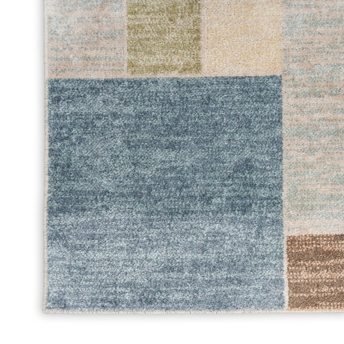 Geometric patchwork area rug with a large blue block surrounded by beige, tan, olive green, and gray tiles.