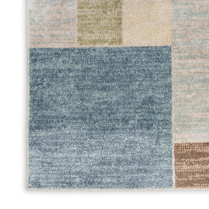 Geometric patchwork area rug with a large blue block surrounded by beige, tan, olive green, and gray tiles.