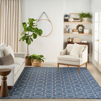 Cozy living room with navy geometric rug, cream sofa and striped armchair, potted plants, and wooden shelves.