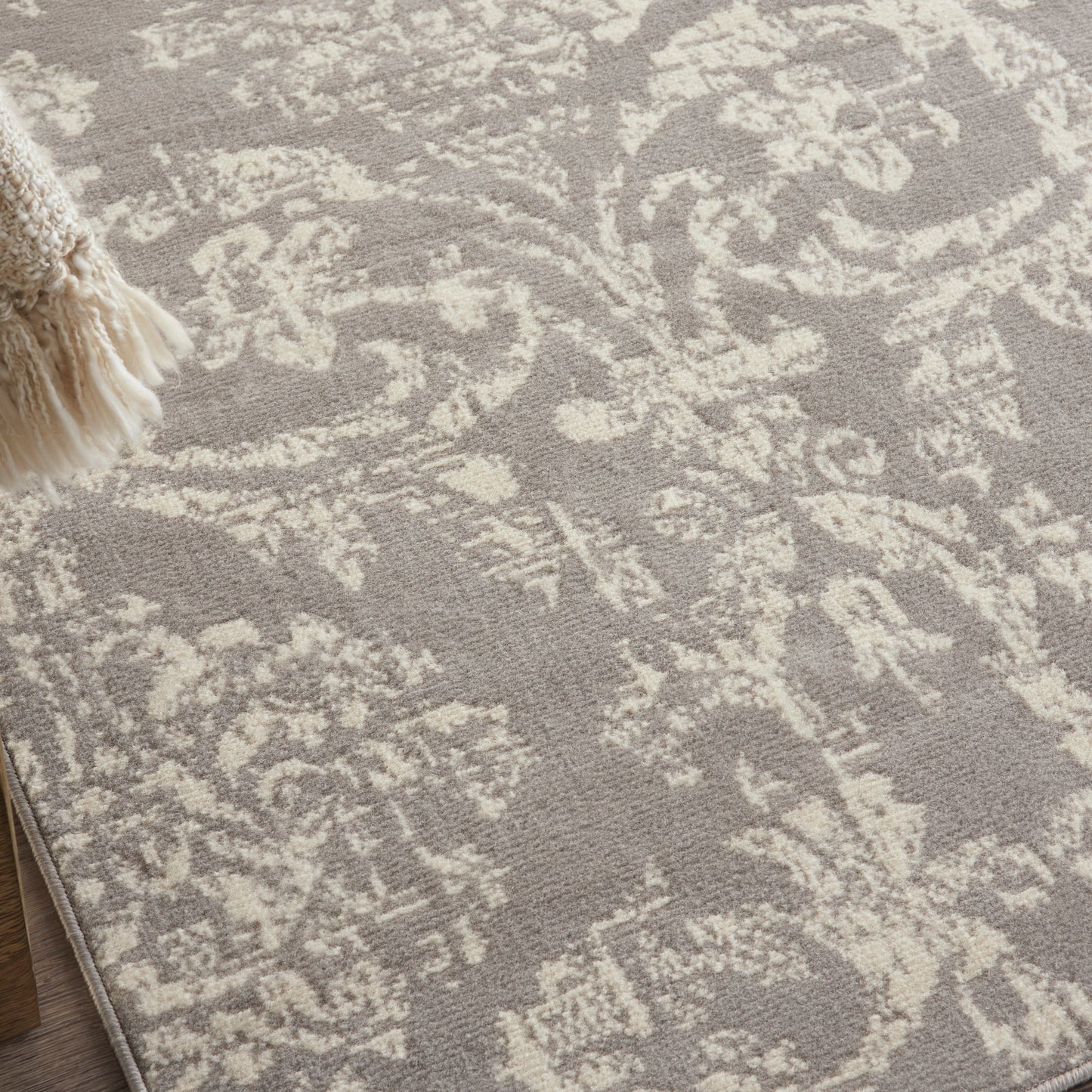 Taupe rug with cream damask floral pattern and fringe tassel trim along the edge.