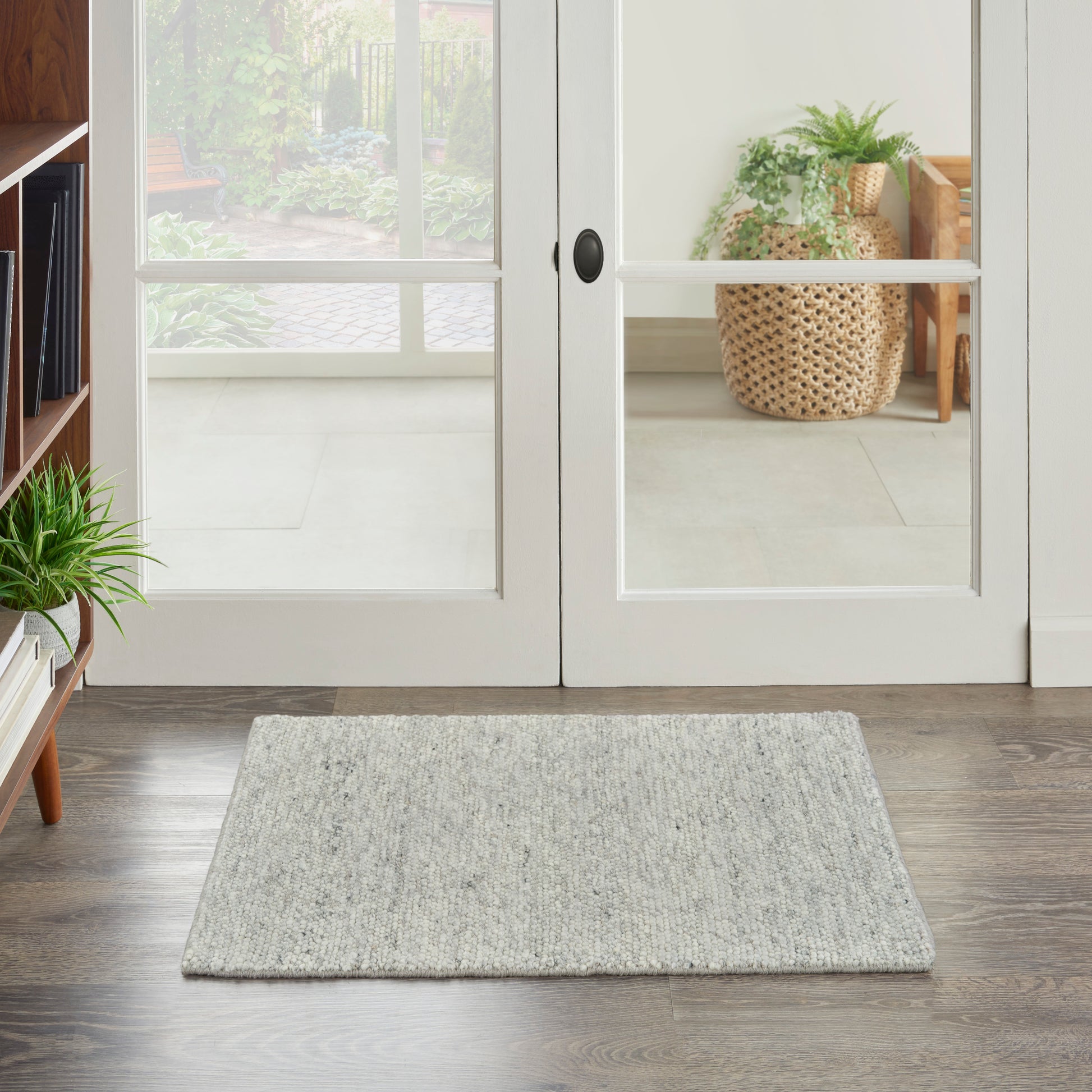 Light gray textured rectangular entry rug on dark wood floor in front of white-framed glass doors; greenery visible.