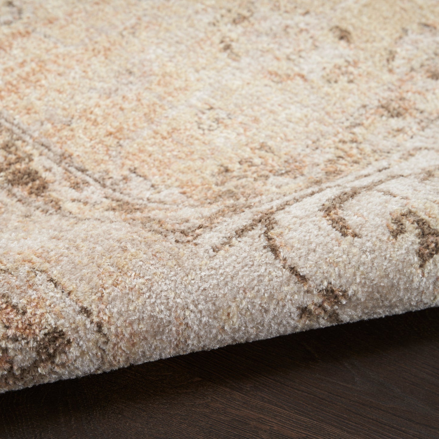 Cream-beige plush area rug with subtle tan pattern and a rolled edge on dark wood flooring.