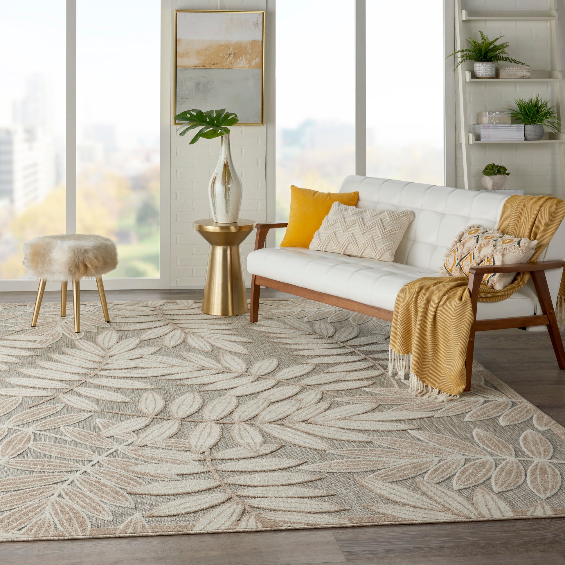 Bright modern living room with white sofa, wooden arms, mustard cushions, gold side table, tropical leaf-pattern rug, fur stool.