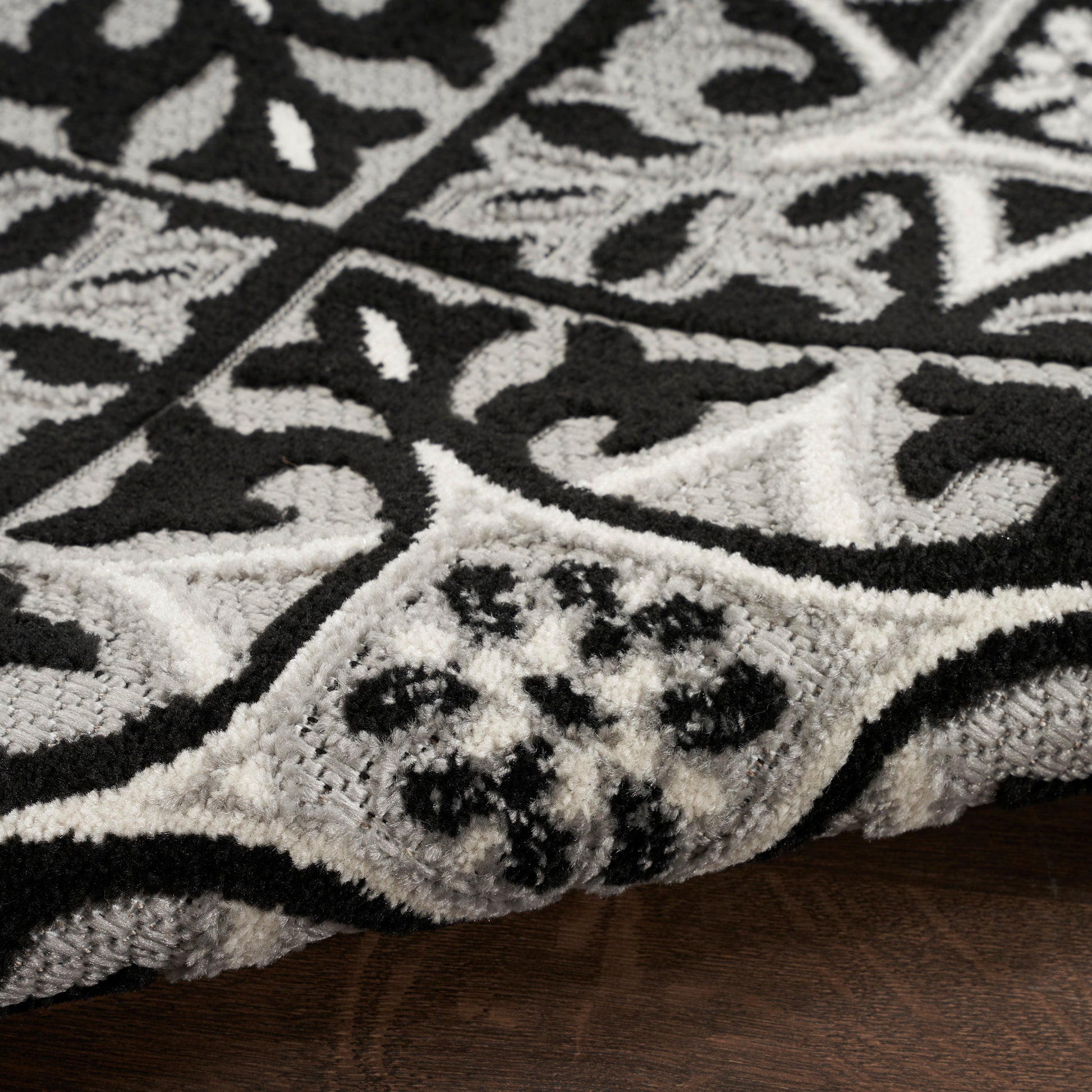 Black and white ornate patterned shag rug with plush pile and curled edge on a wooden floor.
