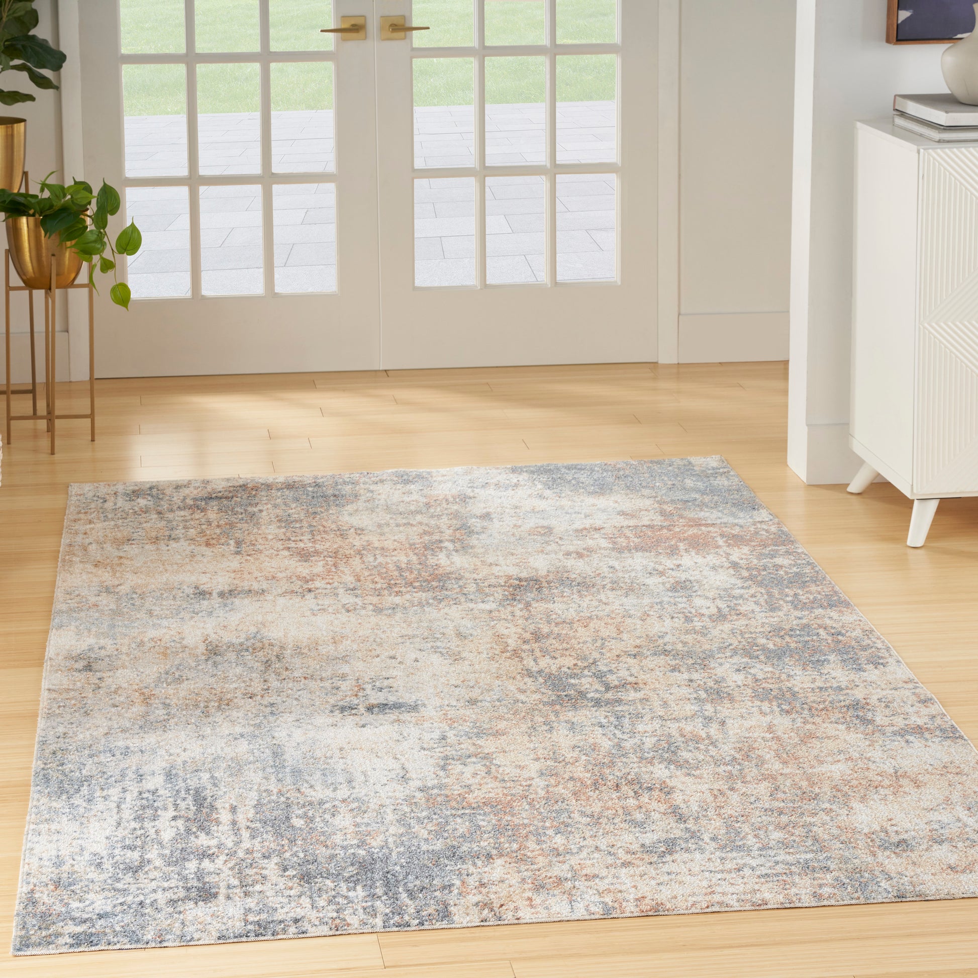 Abstract blue-gray and beige area rug on light wood floor in a bright room.