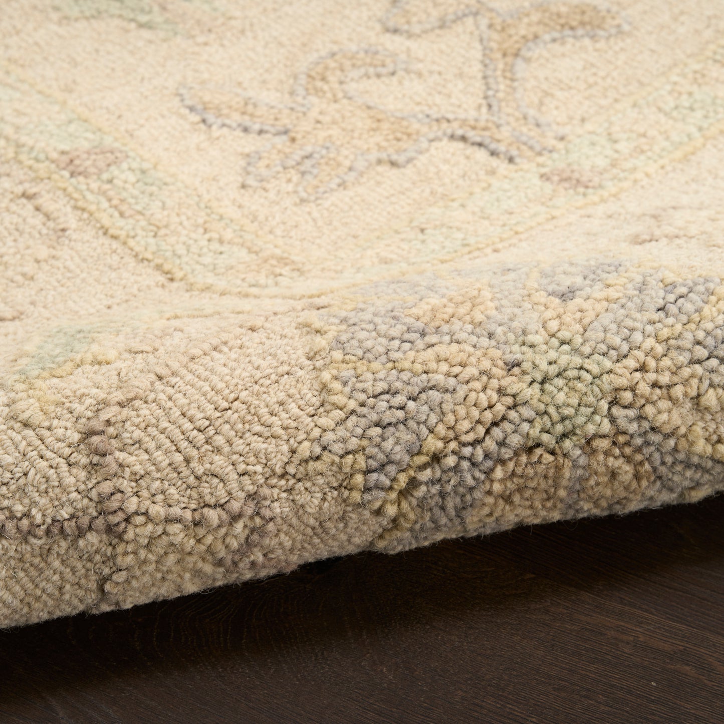 Soft beige rug with subtle pastel floral pattern; dense pile and rolled edge on dark wood floor.