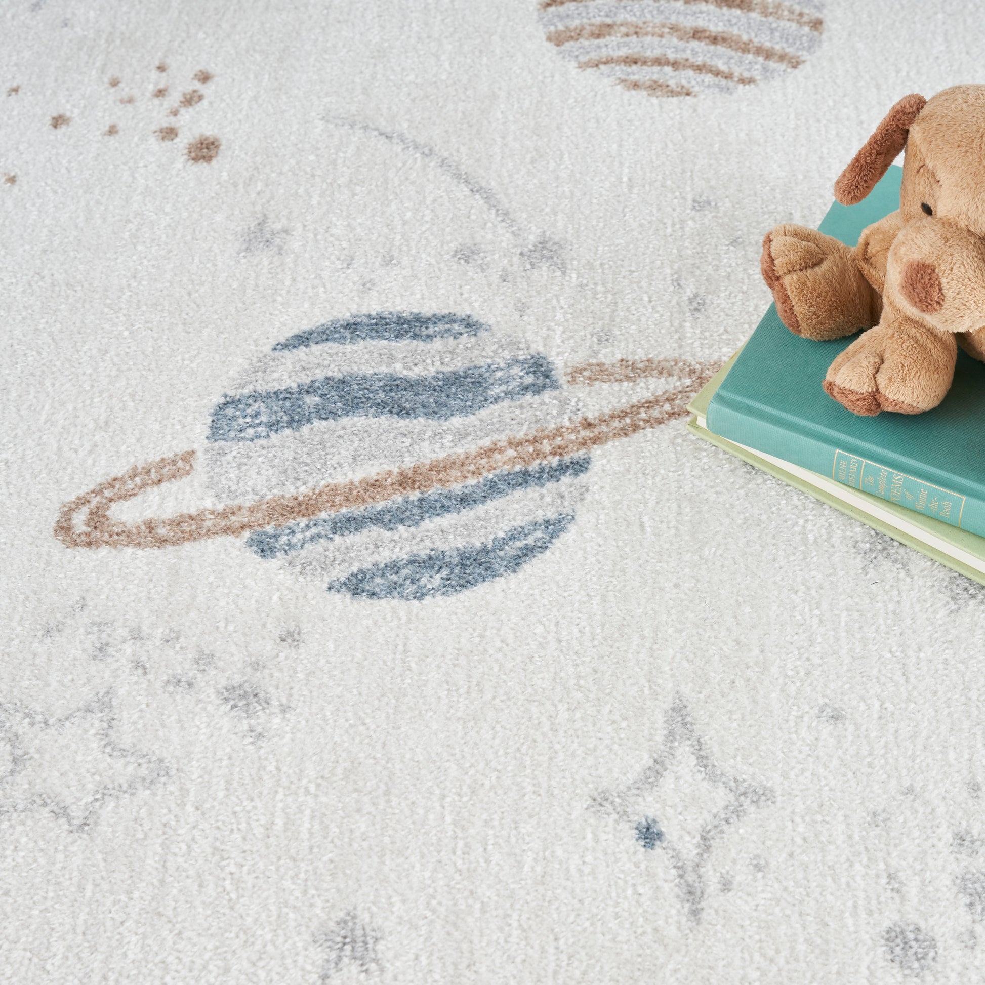 Brown plush teddy bear resting on teal & mint books on a soft white space-pattern rug with planets & stars.