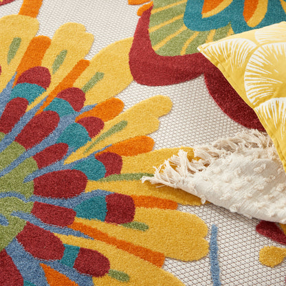 Bright multicolor round floral rug with yellow, teal, orange petals and fringe, alongside a yellow leaf-patterned pillow.