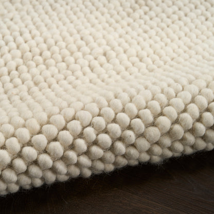 Cream boucle rug with densely packed wool pom-pom texture on dark hardwood floor.