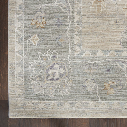 Soft gray-blue rug with ivory floral motifs and a light border on dark wooden floor.