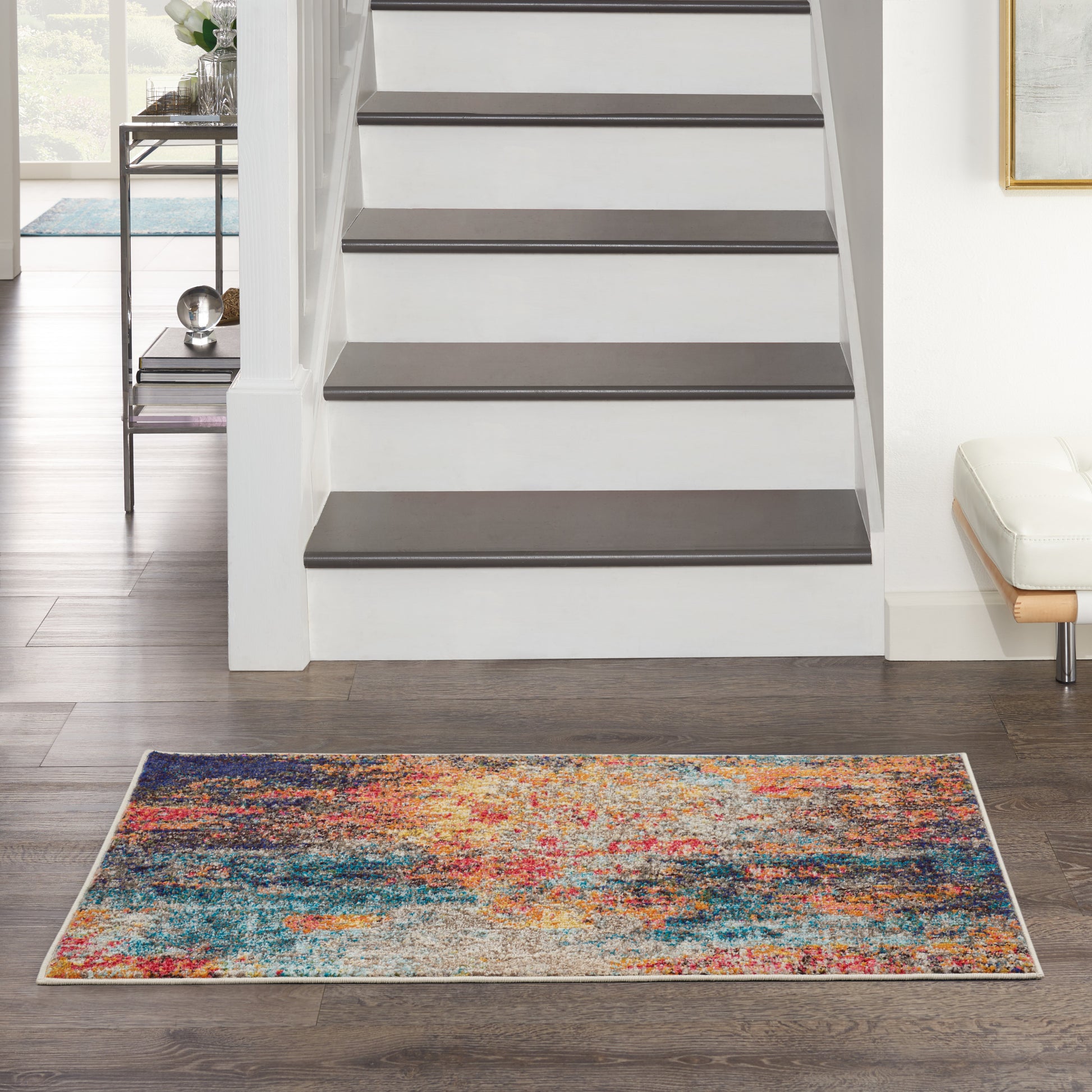 Colorful abstract rug on a dark hardwood floor in a modern home foyer with a white staircase and dark gray treads.