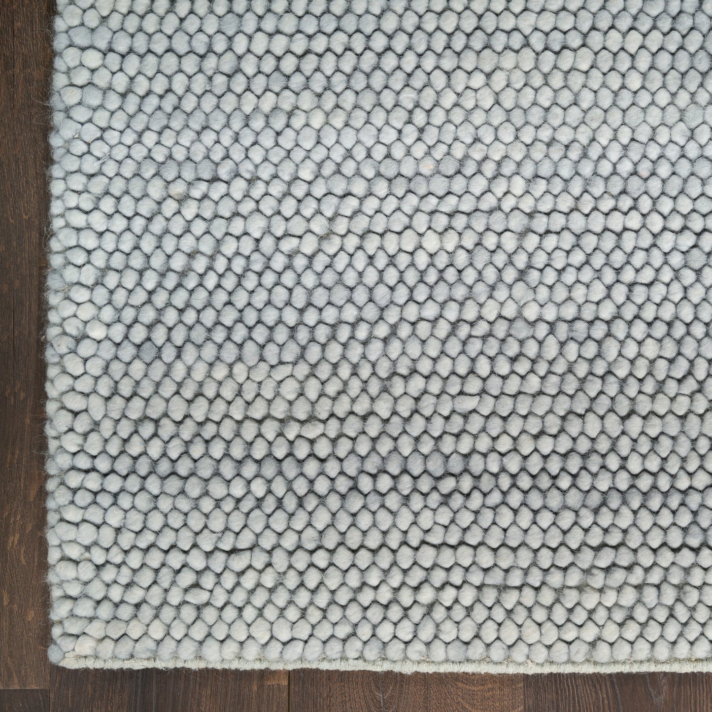 Close-up of light gray looped shag rug edge on dark wood floor; plush, textured area rug.