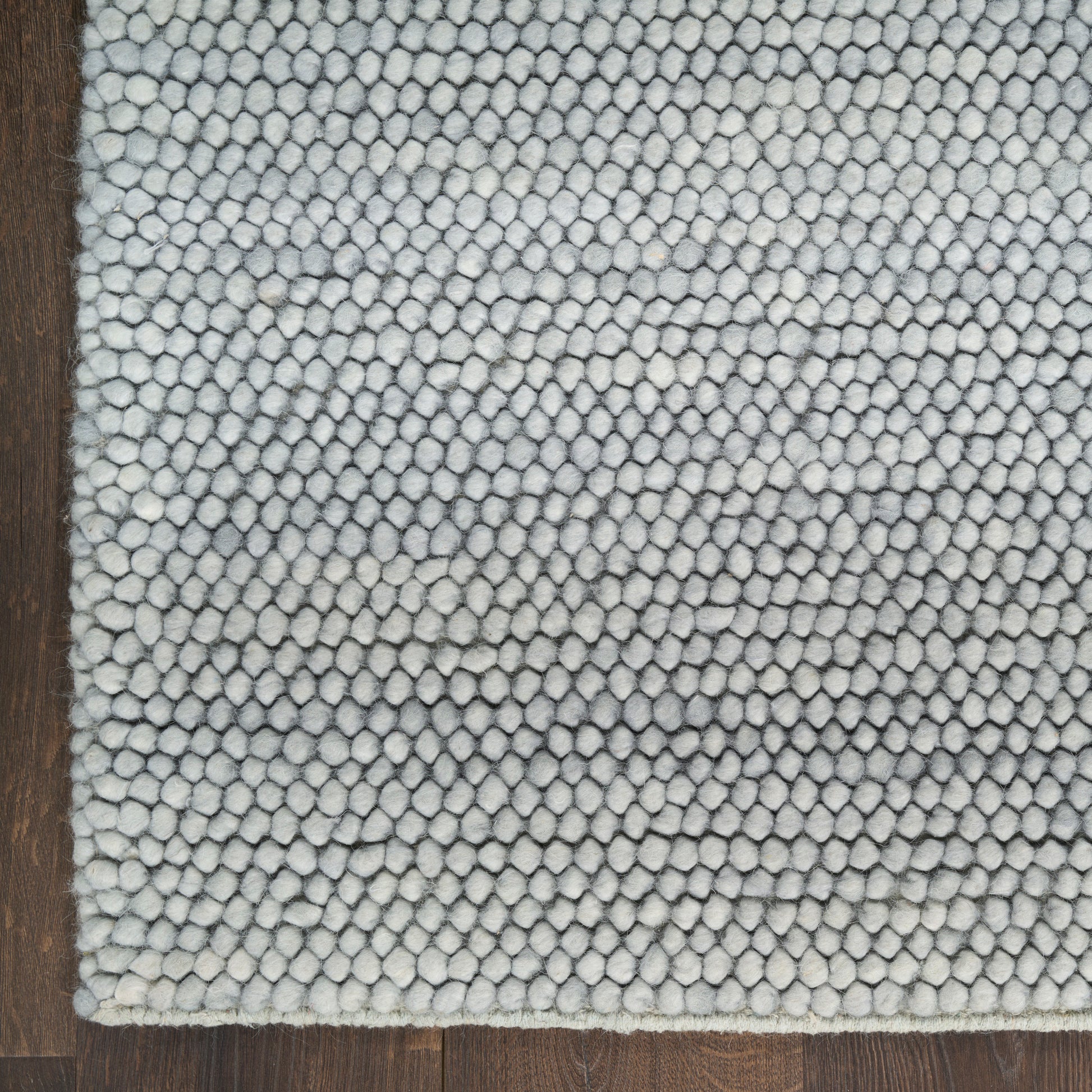 Close-up of light gray looped shag rug edge on dark wood floor; plush, textured area rug.