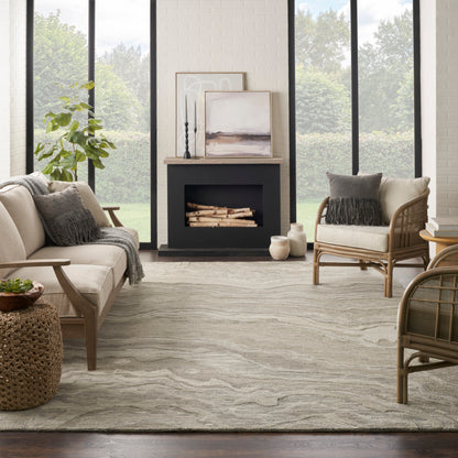 Cozy contemporary lounge with beige sofa, rattan armchairs, neutral rug, fireplace, potted plant, and art by large windows.