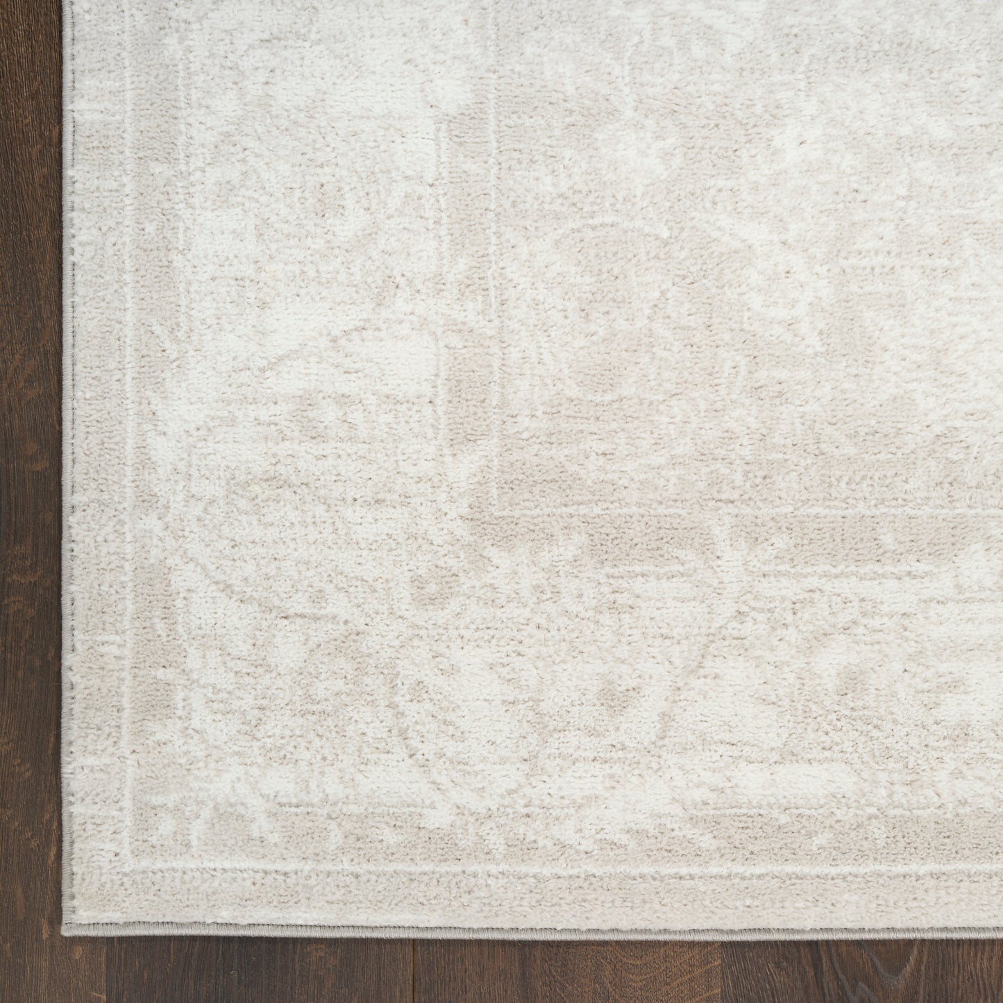 Cream beige rug with subtle damask pattern and border on dark wood floor.
