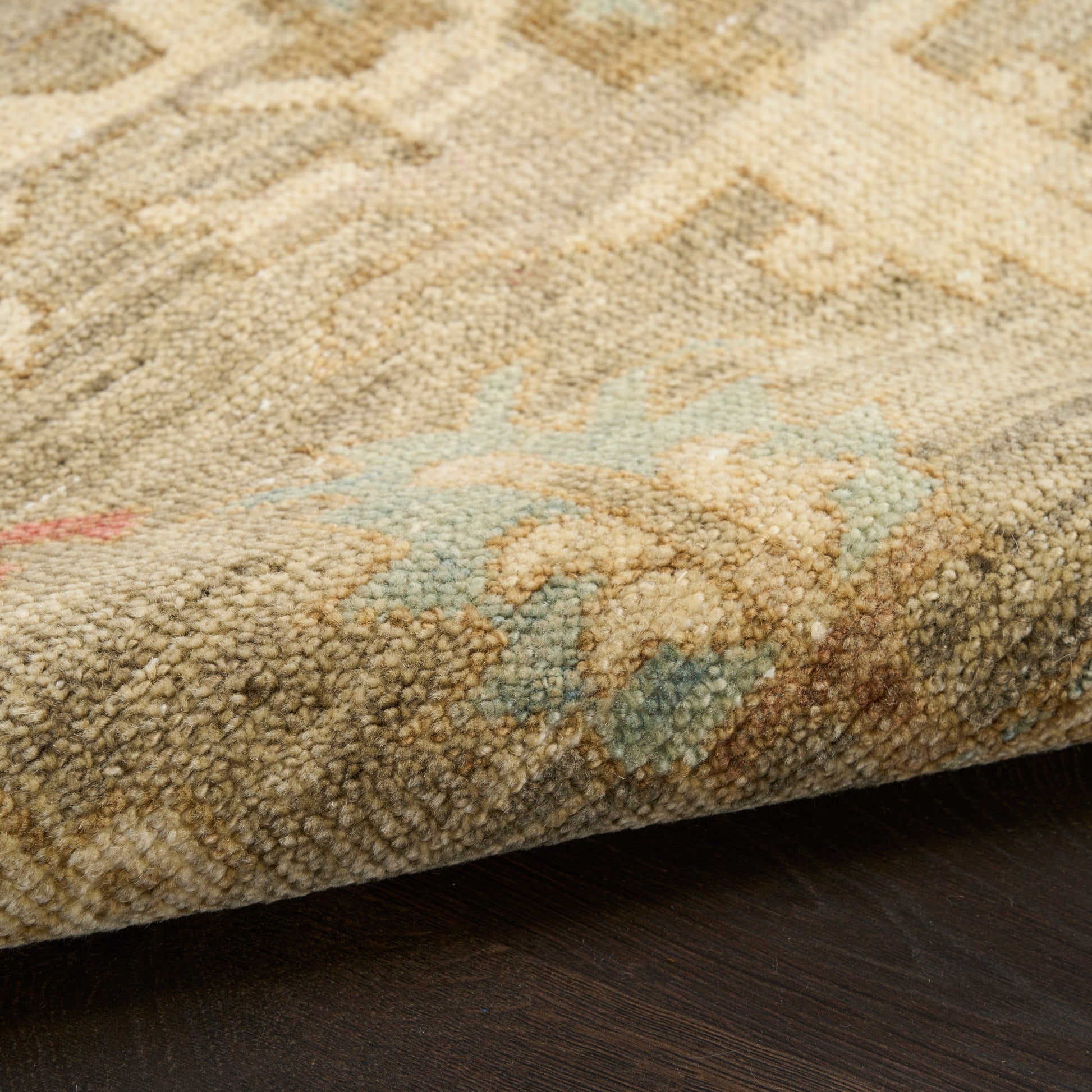 Close-up of a tufted beige oriental rug with pale blue accents and a folded edge on dark wood floor