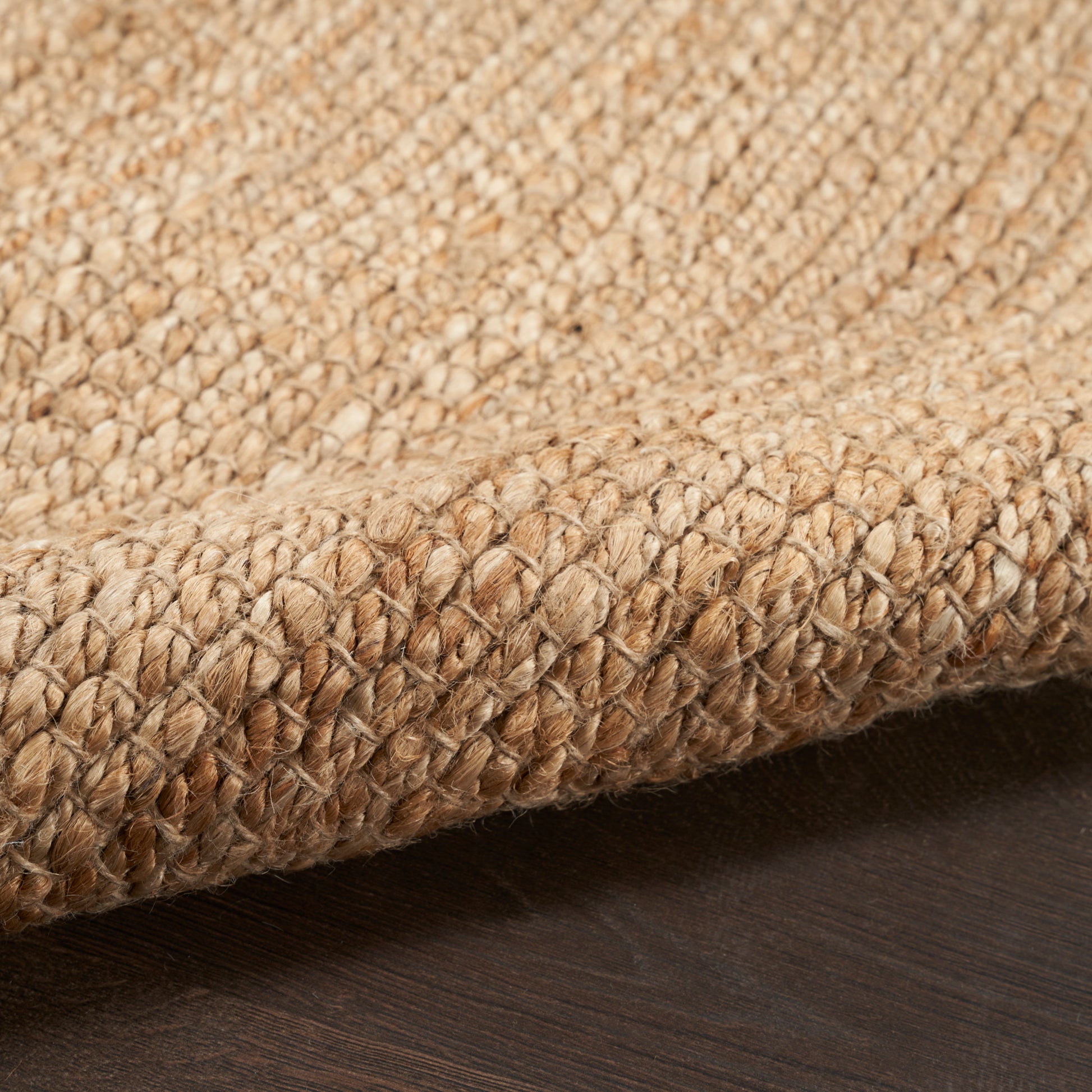 Natural beige jute rug with thick braided texture and folded edge on dark wood floor.