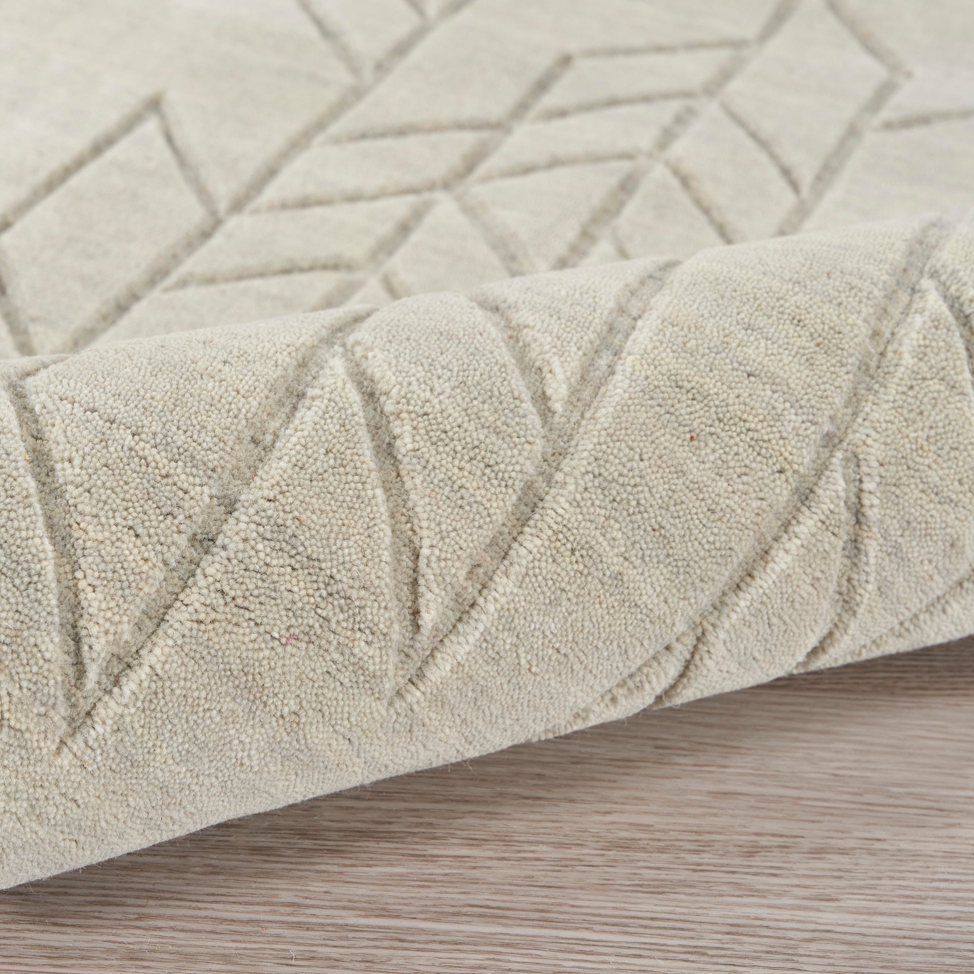 Beige flat-weave rug with geometric chevron and diamond pattern, soft textured pile, rolled edge on wood floor.