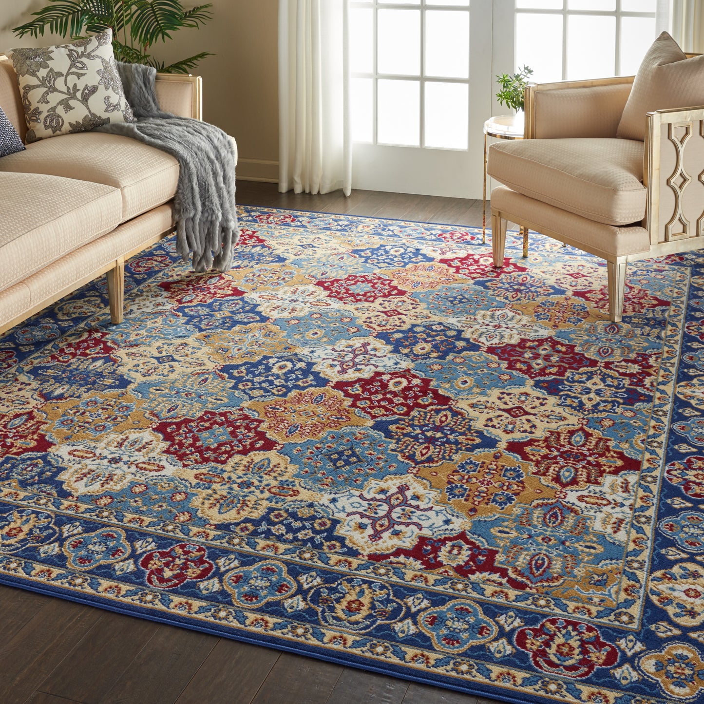 Bohemian patterned area rug in blue, red, gold and cream, in a sunlit living room with beige sofas.