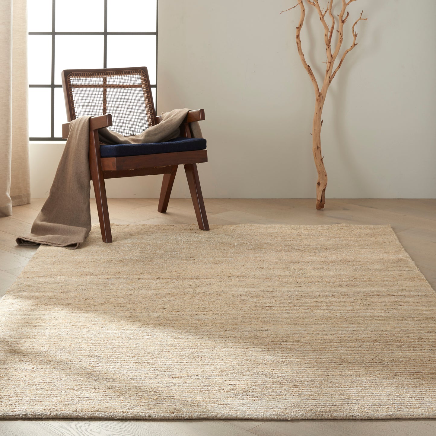 Wooden armchair with cane back, navy cushion, beige throw, on natural jute rug in a light minimalist room.