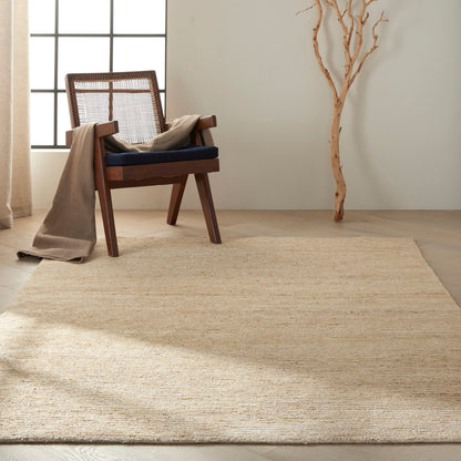 Wooden armchair with cane back, navy cushion, beige throw, on natural jute rug in a light minimalist room.