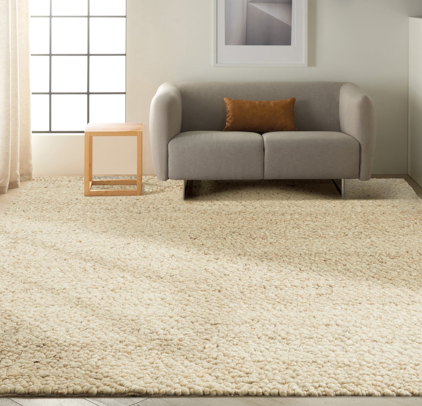 Light gray sofa with rounded arms, brown pillow, on cream shag rug; small wooden cube side table beside a grid-window.
