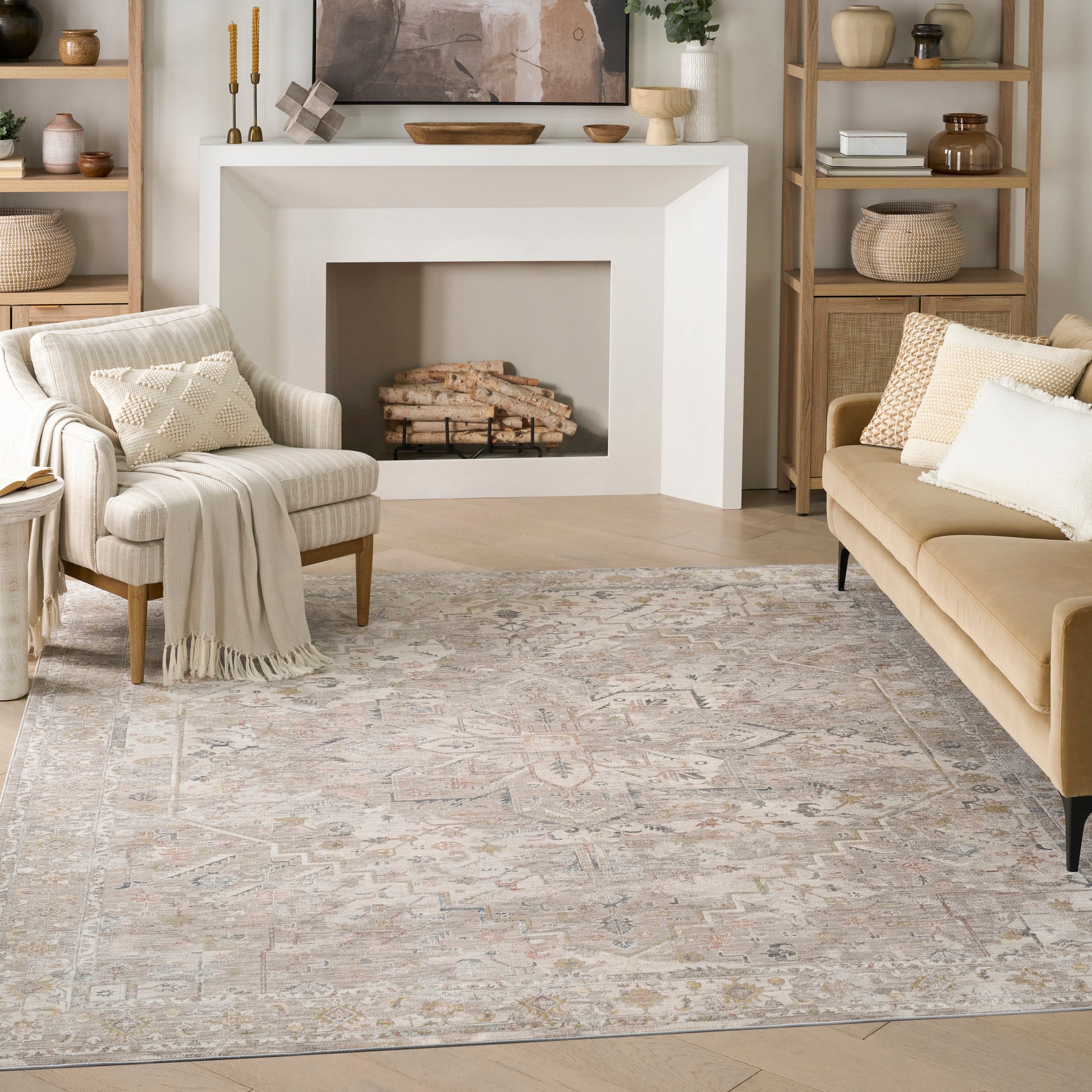 Cozy neutral living room with a large beige patterned rug, white fireplace, beige sofa, striped armchair and wood shelves.