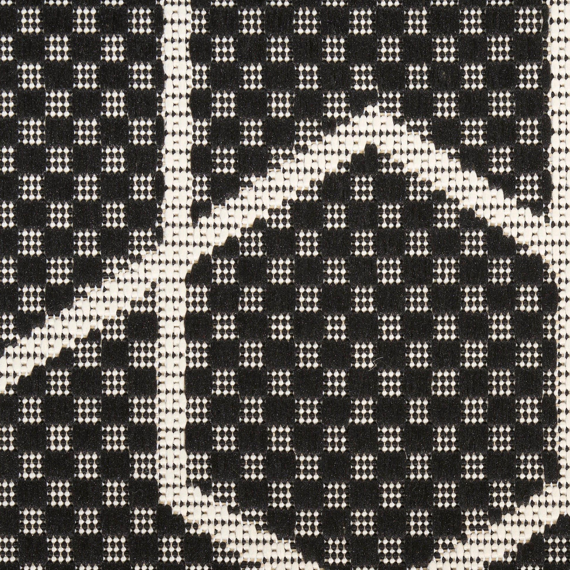 Close-up of black and ivory woven rug with geometric diamond pattern and speckled checker texture.