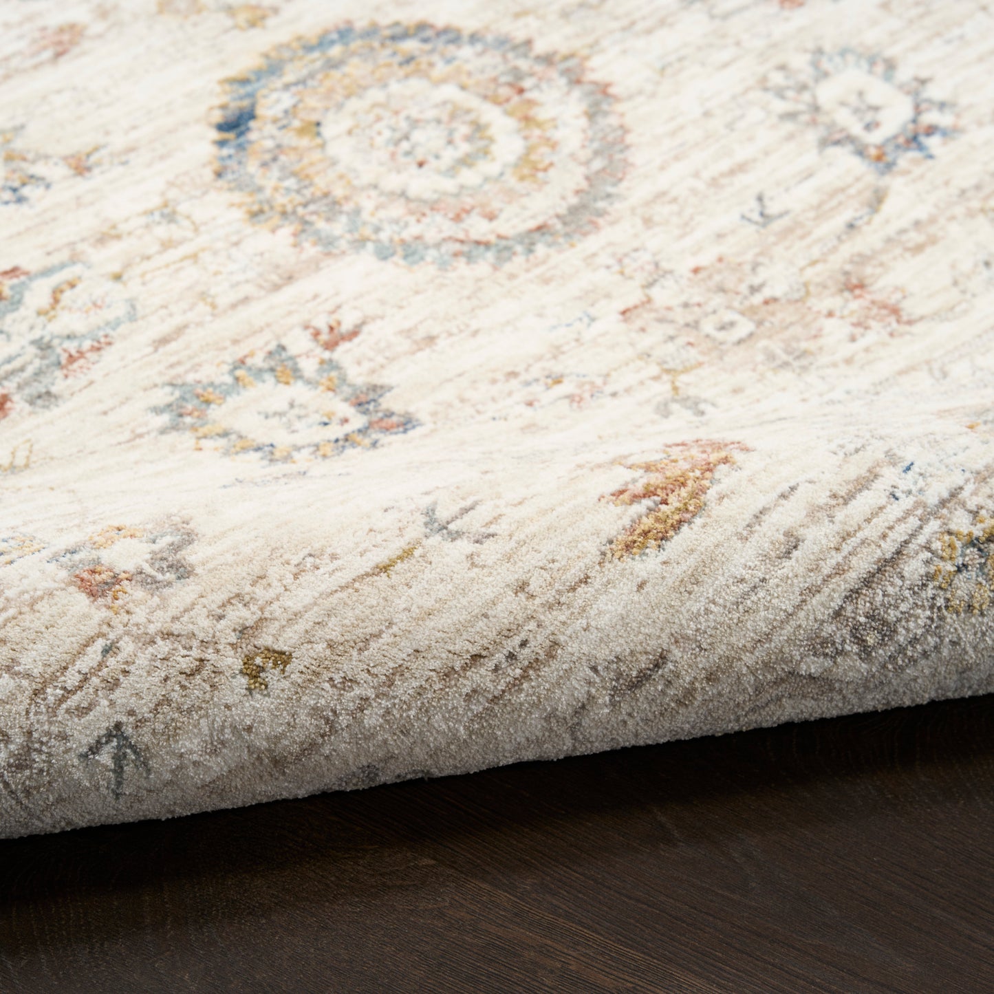 Light beige vintage-style area rug with muted blue, gold and peach circular medallions; folded corner on dark wood.