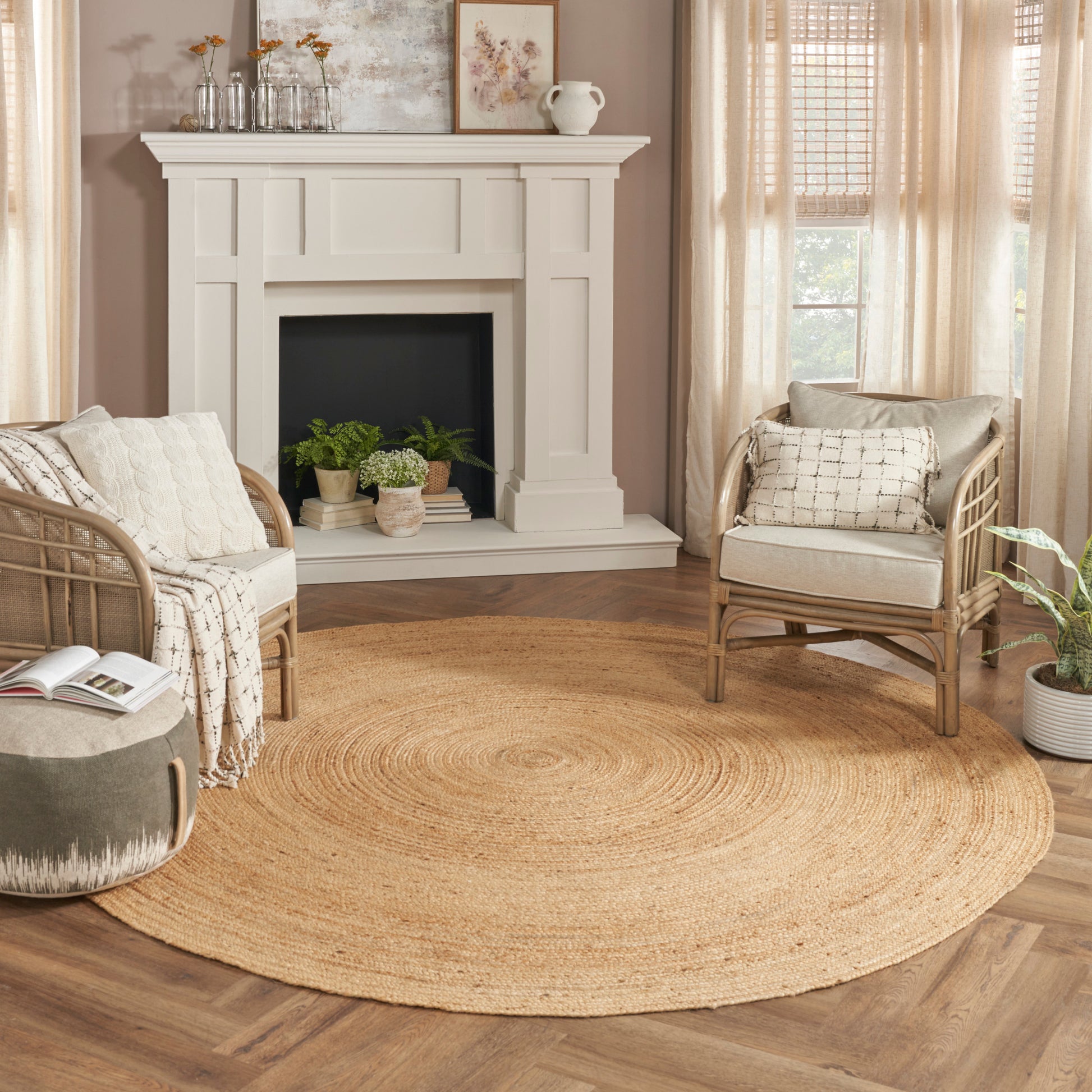 Cozy living room with white mantel fireplace, rattan chairs with cream cushions, and a round braided jute rug with plants.