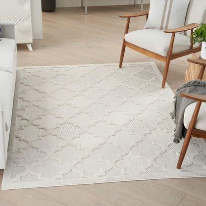 Rectangular cream area rug with a repeating quattrofoil lattice in a bright living room with wooden-framed chairs.