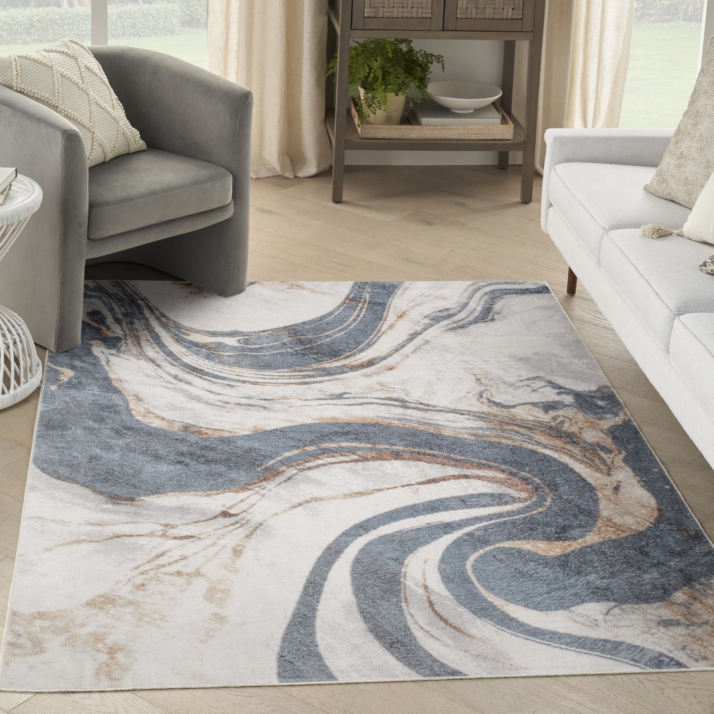 Abstract swirl rug in blue, beige and white on light wood floor, in a cozy living room with gray armchairs and a white sofa.