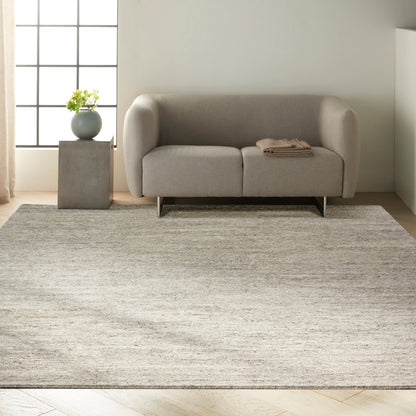 Modern light-gray sofa with rounded arms and metal legs, on a textured beige rug; concrete side table with plant.