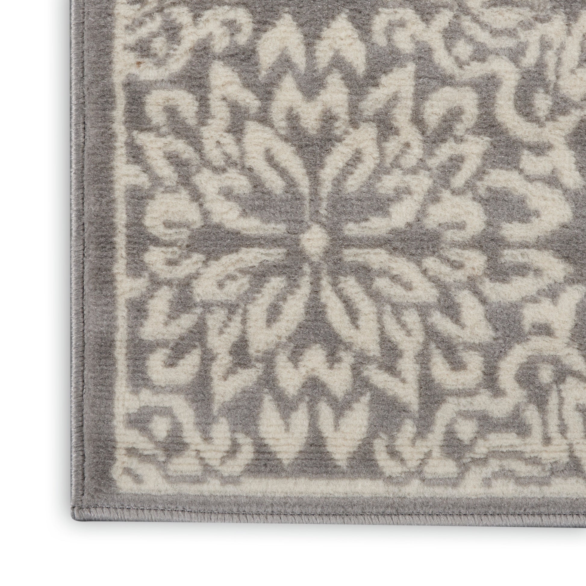 Close-up of a grey and ivory patterned area rug with a central floral/mandala motif and bordered edge.
