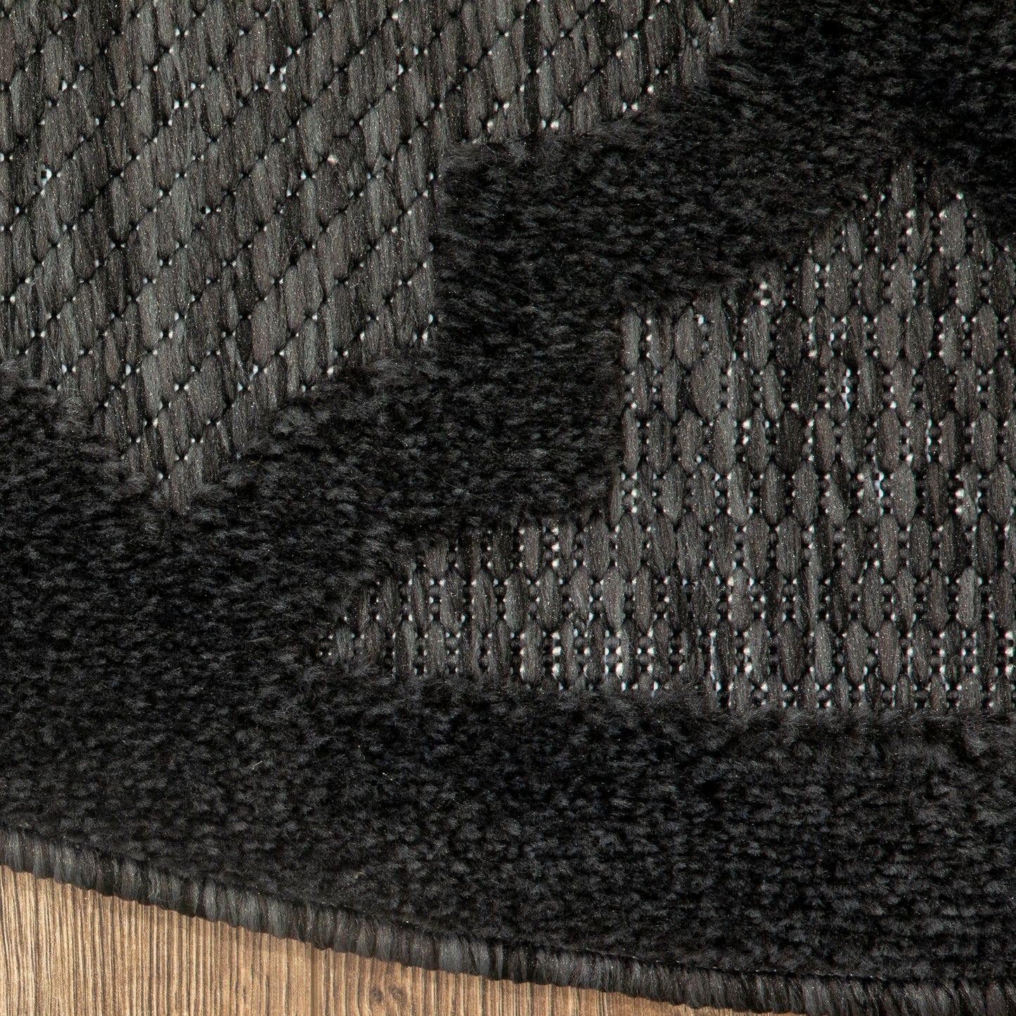 Close-up of black knit fabric with diagonal pattern and plush faux fur trim along the hem of a winter garment.