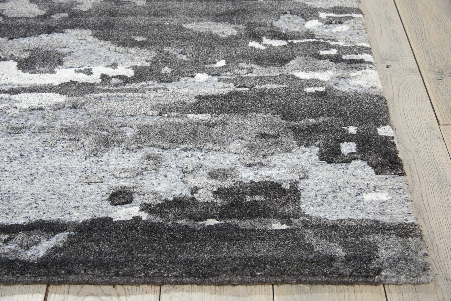 Modern abstract grey-patterned shag rug with charcoal & light grey patches on light wood flooring.